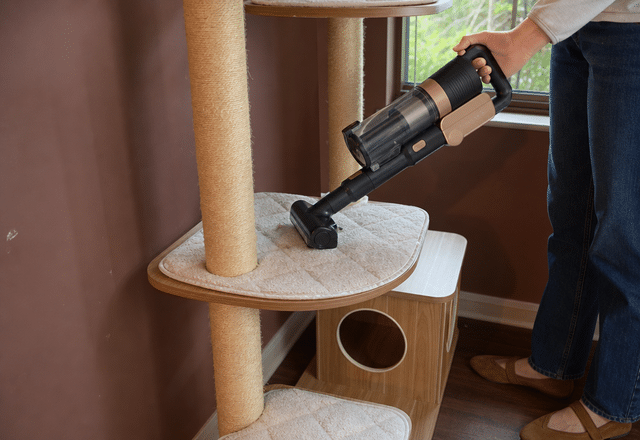 Mini motorized brush attachment vacuuming embedded cat fur off a carpeted cat tree perch
