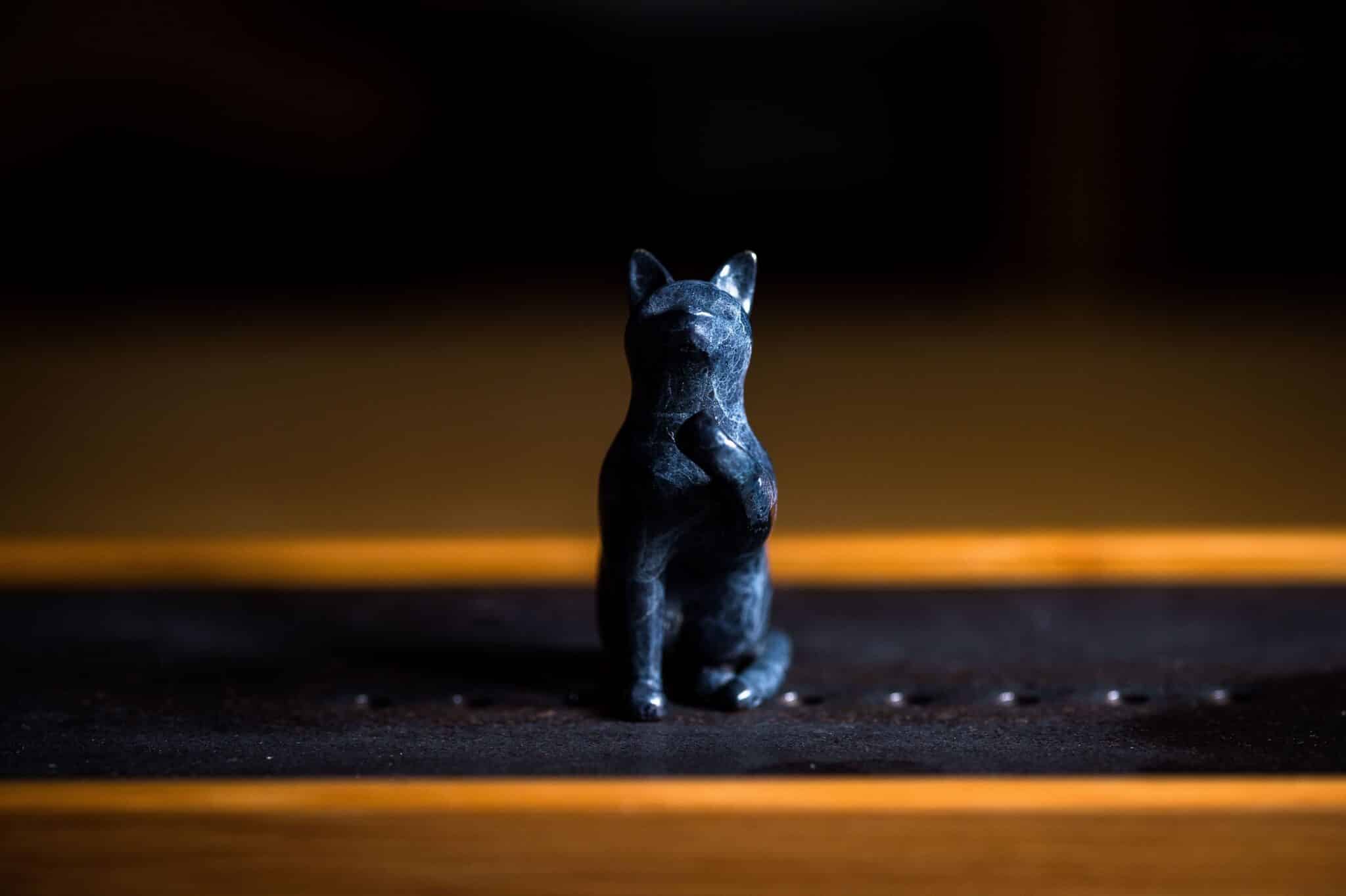 A black cat sitting beside an Egyptian-inspired statue of a seated cat.